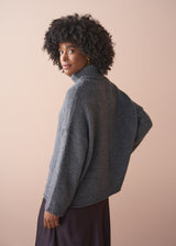 Person wearing a grey chunky knit sweater and satin bias cut skirt against a beige background