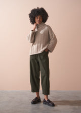 Person wearing a beige fisherman sweater and green barrel leg trousers against a beige background