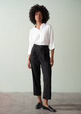 Person wearing a white shirt and black tapered trousers against a plain background