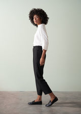 Person wearing a white shirt and black tapered trousers against a plain background