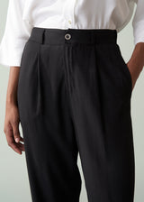 Person wearing a white shirt and black tapered trousers against a plain background