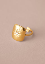 Gold ring with a sun design on a beige background