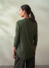 Woman wearing a green long-sleeve top and patterned pants against a neutral background