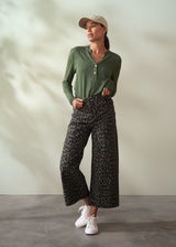 Woman wearing a green top and patterned pants against a neutral background