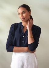 Woman wearing a navy blue shirt and white pants against a neutral background
