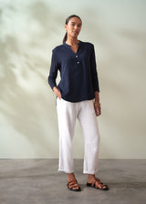Woman wearing a navy shirt and white pants against a neutral background
