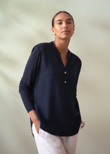 Woman wearing a navy blue shirt with white pants against a plain background