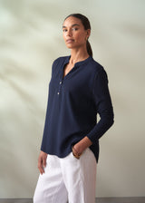 Woman wearing a navy blue shirt and white pants against a neutral background