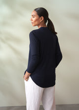 Woman wearing a navy long-sleeve top and white pants against a beige wall.