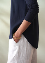 Person wearing a navy blue top and white pants with gold bracelets on a plain background