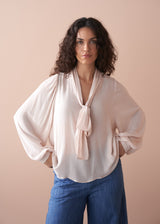 Woman wearing a light pink pussybow blouse and blue wide leg jeans against a beige background