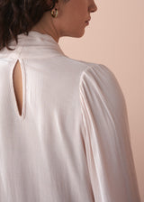 Woman wearing a light pink pussybow blouse and blue wide leg jeans against a beige background