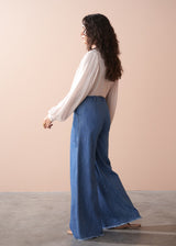 Woman wearing a light pink pussybow blouse and blue wide leg jeans against a beige background