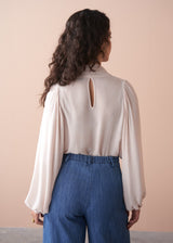 Woman wearing a light pink pussybow blouse and blue wide leg jeans against a beige background