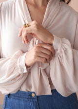 Woman wearing a light pink pussybow blouse and blue wide leg jeans against a beige background