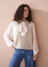 Woman wearing a light pink pussybow blouse and blue wide leg jeans against a beige background