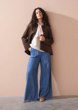 Woman wearing a light pink pussybow blouse and blue wide leg jeans against a beige background