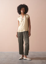 Woman wearing a light yellow satin blouse and green satin trousers against a beige background