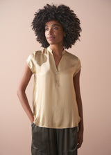 Woman wearing a light yellow satin blouse and green satin trousers against a beige background