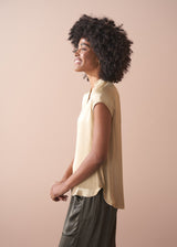 Woman wearing a light yellow satin blouse and green satin trousers against a beige background