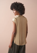 Woman wearing a light yellow satin blouse and green satin trousers against a beige background