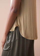 Woman wearing a light yellow satin blouse and green satin trousers against a beige background