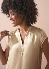 Woman wearing a light yellow satin blouse against a beige background