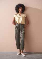 Woman wearing a light yellow satin blouse and green satin trousers against a beige background