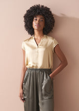 Woman wearing a light yellow satin blouse and green satin trousers against a beige background