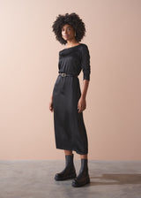 Woman wearing a black satin dress standing against a beige background