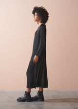 Woman wearing a round neck black straight line satin dress standing against a beige background