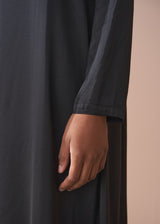 Close up of woman wearing a black satin dress standing against a beige background