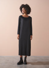 Woman wearing a round neck, black straight line satin dress standing against a beige background