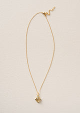 A delicate gold chain necklace with a small, polished gold heart pendant, displayed against a textured off-white background.
