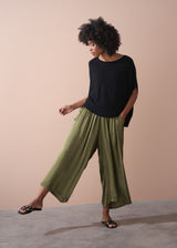 Woman wearing a black top and green wide leg satin trousers against a beige background