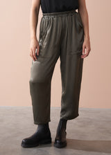 Woman wearing a black camisole top and olive green satin trousers against a beige background