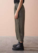 Woman wearing a black camisole top and olive green satin trousers against a beige background