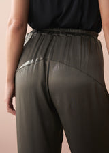 Woman wearing a black camisole top and olive green satin trousers against a beige background