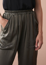 Woman wearing a black camisole top and olive green satin trousers against a beige background