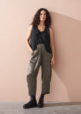 Woman wearing a black camisole top, waistcoat and olive green satin trousers against a beige background