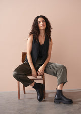 Woman wearing a black camisole top and olive green satin trousers against a beige background