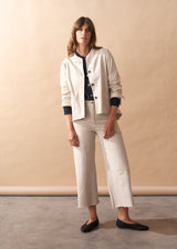 Woman wearing a cream jacket with black buttons against a beige background