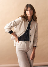 Woman wearing a cream jacket with black buttons against a beige background
