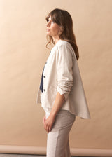 Woman wearing a cream jacket with black buttons against a beige background