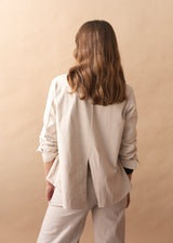 Woman wearing a cream jacket with black buttons against a beige background