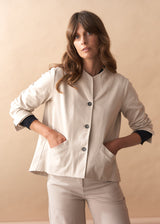 Woman wearing a cream jacket with black buttons against a beige background