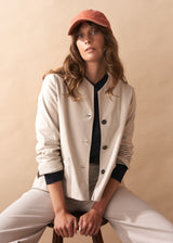 Woman wearing a cream jacket with black buttons against a beige background