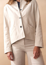 Woman wearing a cream jacket with black buttons against a beige background