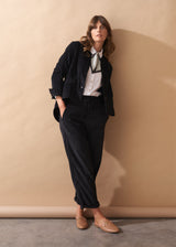 Woman in a black corduroy suit standing against a beige wall