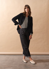 Woman wearing a black jacket and dark pants against a beige wall